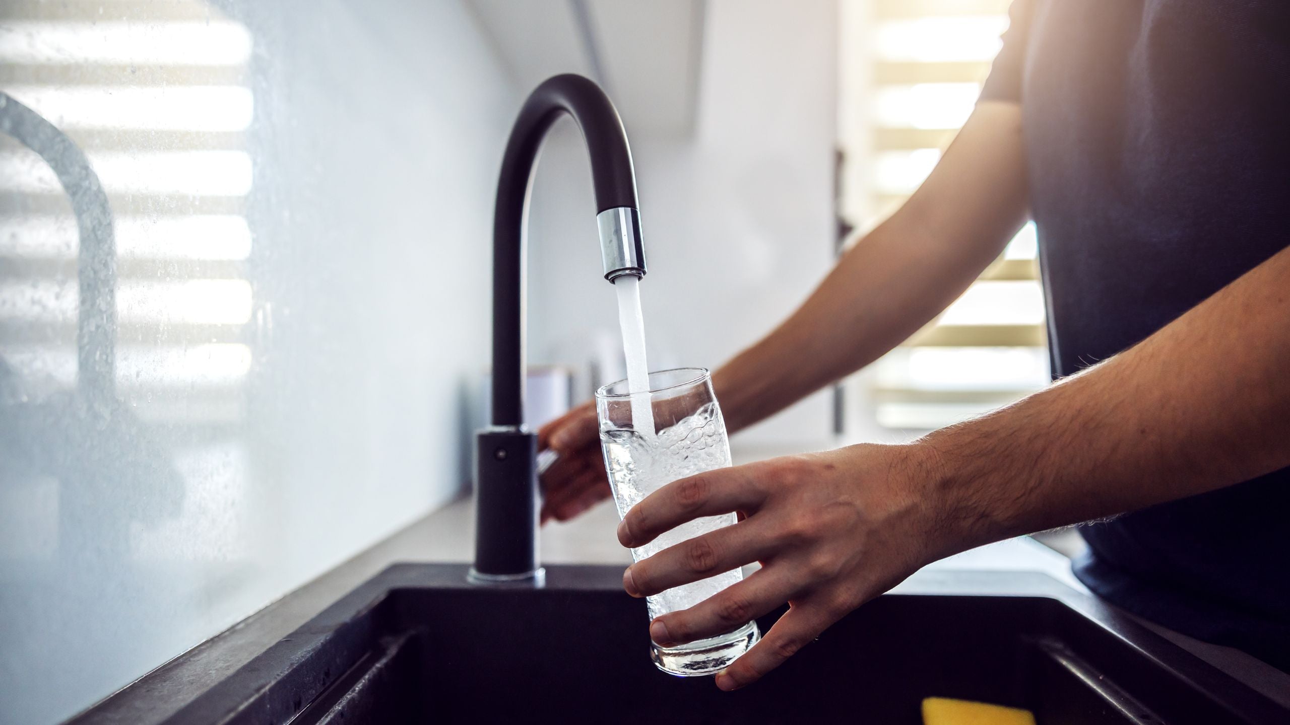 Person filling a glass with water from a modern kitchen faucet.
