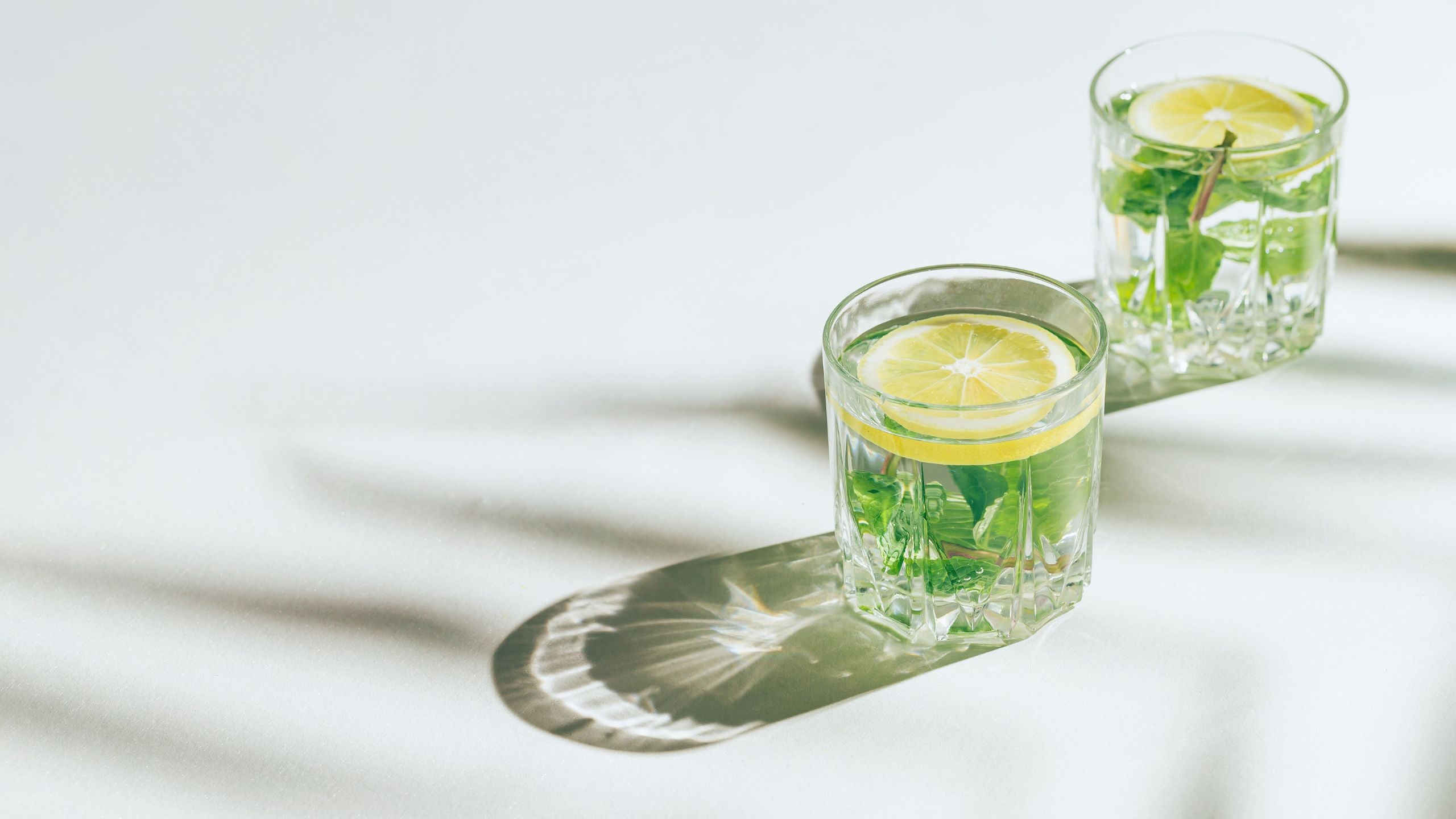 Two glasses of lemon water with mint leaves on a white surface